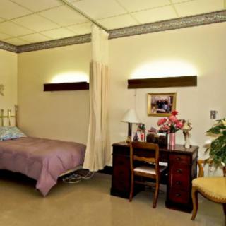 A cozy hospital room with a bed, desk, and seating area.