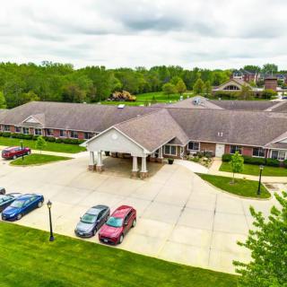 Aerial view of a building with a parking lot surrounded by greenery on an overcast day.