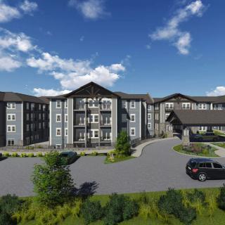 A modern apartment complex with landscaped surroundings and a spacious parking area under a clear blue sky.
