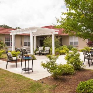 A well-maintained patio area with outdoor seating and a pergola, surrounded by lush greenery.