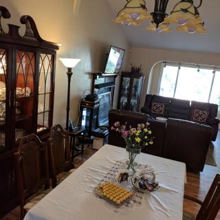 A cozy dining and living area with a table set for entertaining, featuring flowers, comfortable seating, and a television.