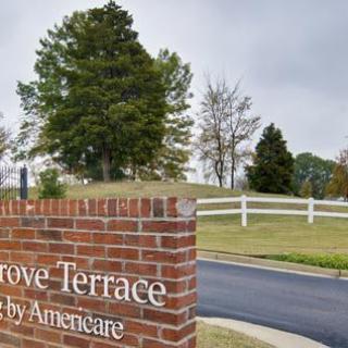 A brick signpost in front of a landscaped area with trees and a white fence.