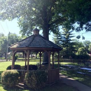 A charming gazebo nestled in a lush park, surrounded by greenery and sunlight.