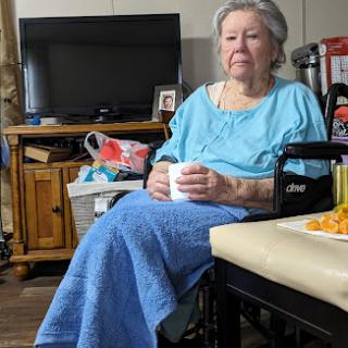 An elderly woman sitting in a wheelchair, enjoying a warm drink in her cozy living room.