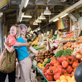Two friends enjoying a vibrant day at the market surrounded by fresh produce.
