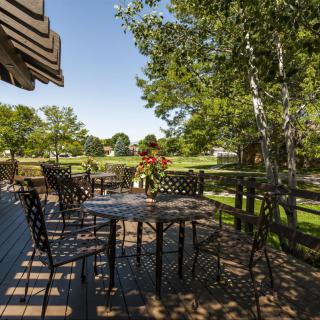A sunny outdoor patio with tables and chairs, surrounded by lush greenery.