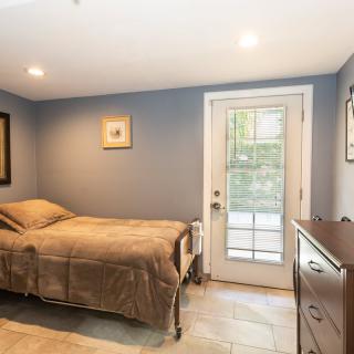 A cozy bedroom with a single bed, soft lighting, and a door leading outside.