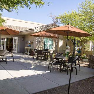 A sunny outdoor patio with tables, chairs, and umbrellas next to a building.