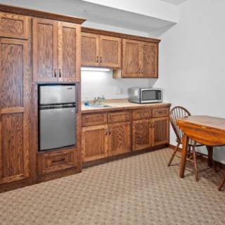 A small kitchen area with wooden cabinets, a mini fridge, microwave, and a dining table.