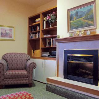 A cozy living room with a fireplace and an armchair, featuring a bookshelf filled with books and decorative artwork.