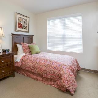 A cozy bedroom with a single bed, wooden furniture, and a window letting in natural light.