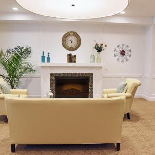 A cozy living room with plush beige sofas facing a white fireplace, adorned with decorative items and a wall clock.