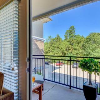 A cozy balcony with outdoor seating overlooking a view of trees under a clear, sunny sky.