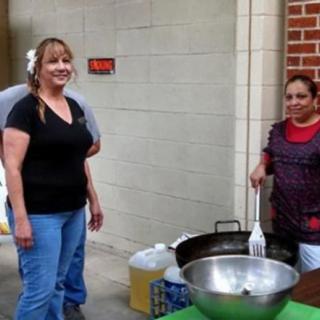 Two people are engaged in outdoor food preparation at an event.