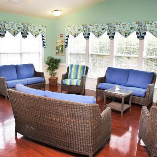 A cozy living room with wicker furniture, blue cushions, and large windows.
