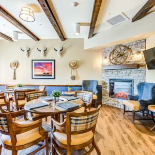 A cozy restaurant dining area with wooden tables and chairs, decorated with a stone fireplace and wall art.