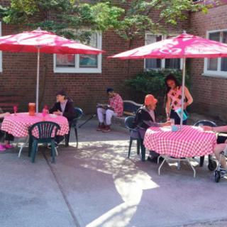 People sitting at an outdoor cafe with red umbrellas and checkered tablecloths.