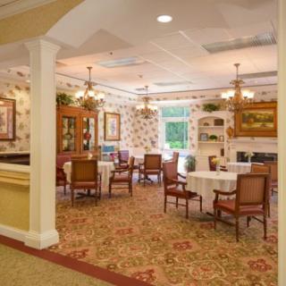 A warmly decorated dining room with tables and chairs, featuring decorative wallpaper and carpet.