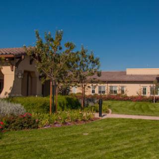 A beautiful landscape featuring well-manicured grass and trees surrounding a charming building under a clear blue sky.