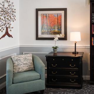 A cozy living room corner featuring an armchair, a small table with a lamp, and colorful artwork on the wall.