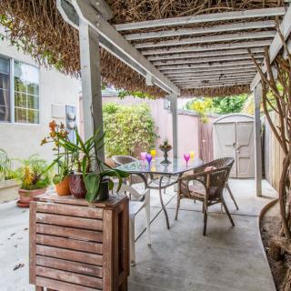 A cozy outdoor patio with a rustic pergola, featuring a dining table and chairs surrounded by lush plants.