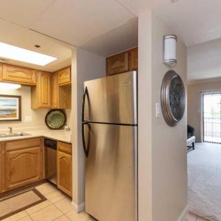 A modern apartment kitchen with wooden cabinets and a stainless steel fridge adjacent to an open living area.