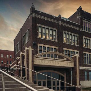 A historic brick building with large windows and a decorative entrance, set against a dramatic sky.
