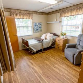 A cozy, well-lit hospital room featuring a patient bed, comfortable chair, and warm wooden flooring.