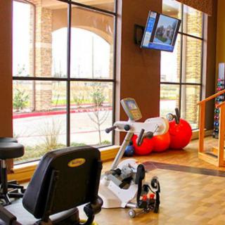 A well-lit gym area featuring a stationary bike, treadmill, and medicine balls with a window view and television.
