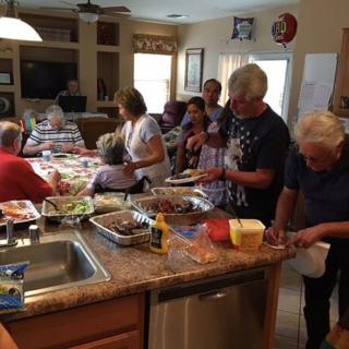 A family gathers in the kitchen for a shared meal, with various dishes laid out on the counter.