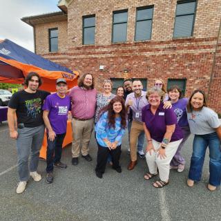 A group of people gathered outdoors in front of a brick building, smiling and enjoying an event.