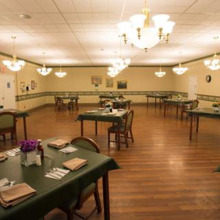 An empty dining room with neatly set tables, wooden floors, and overhead chandeliers.