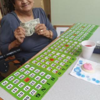 An elderly woman happily holding money after winning a bingo game.