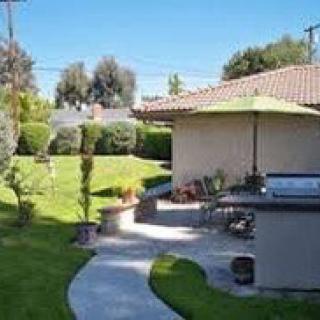 A well-maintained backyard with a patio and green lawn, featuring outdoor furniture under an umbrella.
