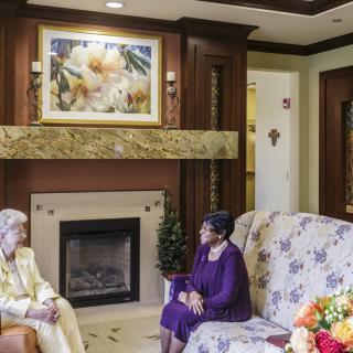 Two women having a conversation in a cozy living room with a fireplace.
