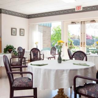 A brightly lit dining area with round tables, chairs, and floral centerpieces.