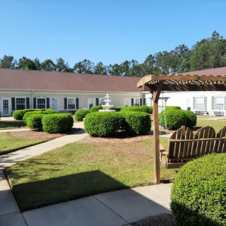 A well-manicured courtyard with a pergola and neatly trimmed bushes against a clear blue sky.