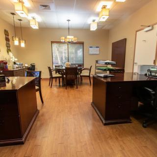 A well-organized office space with wooden flooring and multiple desks, featuring overhead lighting and a large window at the back.