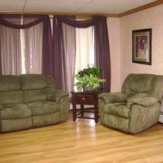 A cozy living room with green furniture, hardwood flooring, and decorative curtains.