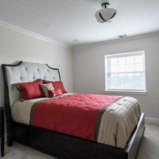 A neatly arranged bedroom with red and beige bedding, featuring a large window that allows natural light to brighten the room.