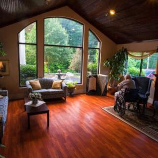 A cozy living room filled with natural light, featuring large windows, wooden flooring, and comfortable furniture.