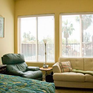 A cozy living room featuring a green armchair, beige couch, and large windows allowing natural light to fill the space.