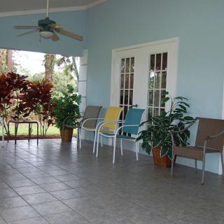 A serene porch with colorful chairs, potted plants, and a ceiling fan creates a welcoming outdoor space.