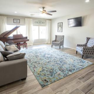 A bright and inviting living room featuring a piano, comfortable seating, and a decorative rug.