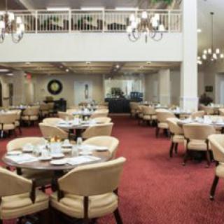 A spacious dining area with round tables and cushioned chairs, featuring elegant chandeliers and a red carpeted floor.