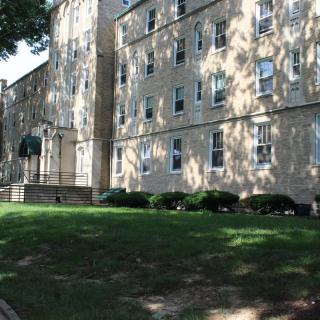 A residential building with multiple floors surrounded by trees and grass.