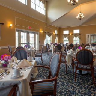 An elegant dining room setup with neatly arranged tables and chairs, adorned with flowers.