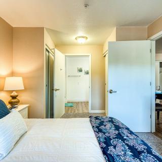 A cozy bedroom with a neatly made bed, a bedside lamp, and open doors leading to other rooms.