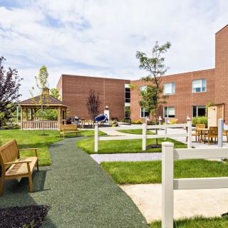 A landscaped garden with pathways, benches, and trees adjacent to a brick building.