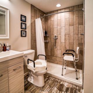 An accessible bathroom features a walk-in shower with a chair and handrails.